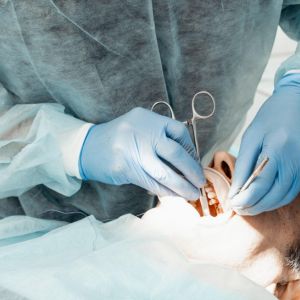 Dentist in gloves and gown performing a dental procedure on a patient using dental instruments inside the mouth