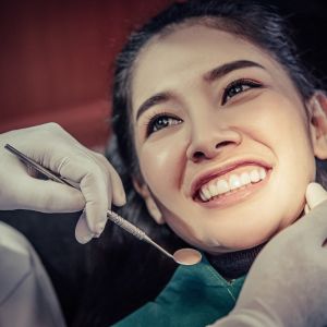 Smiling woman in a dental chair as a clinician with gloved hands uses a dental instrument nearby
