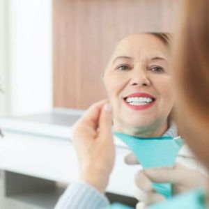 Dental hygienist in gloves adjusts a blue bib on a smiling patient during a dental exam in a clinic