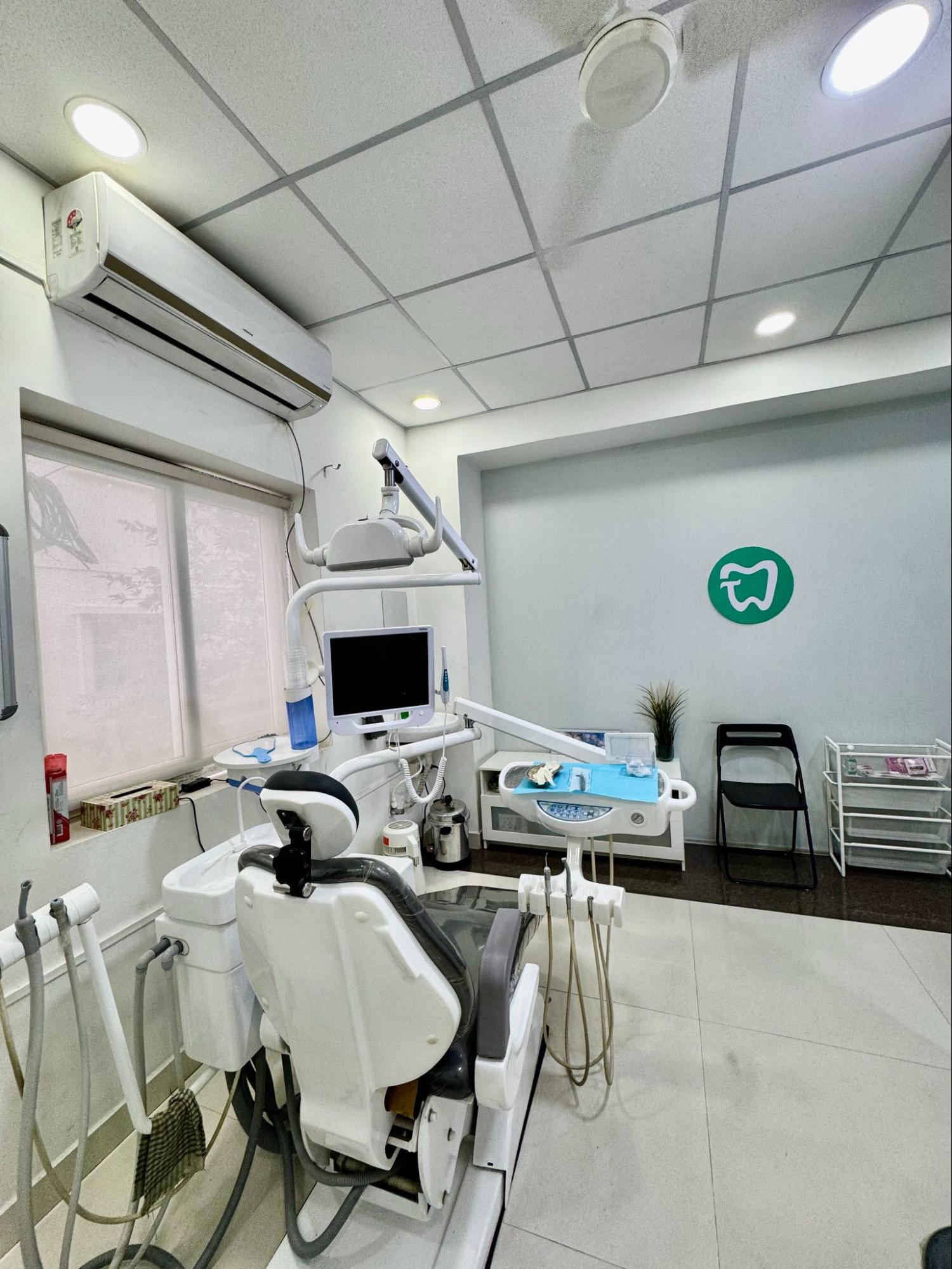 Dental clinic treatment room with a dental chair monitor and overhead light equipment near a window and air conditioner on the wall