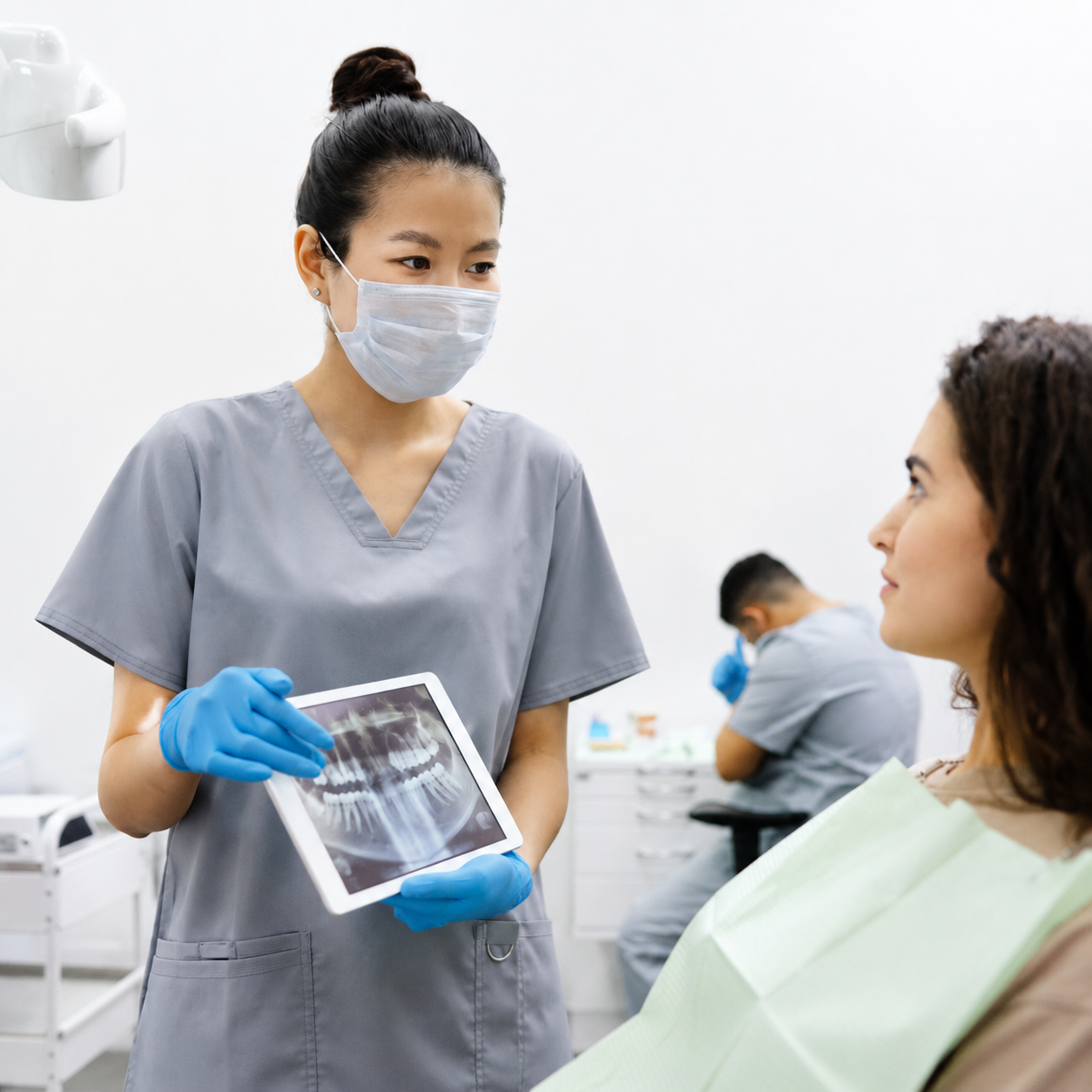 Dental professional in scrubs and mask shows a dental X ray to a patient in a clinic