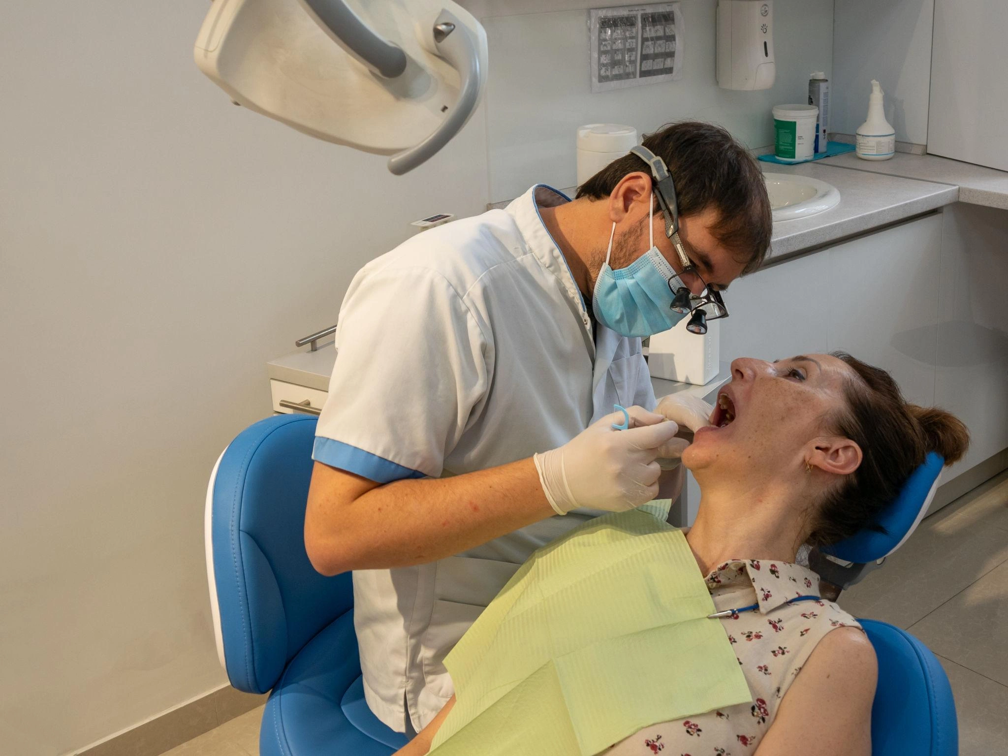 ConsultationOralHealthCheckUp truewhite Dentist in a mask and gloves leaning over a patient in a dental chair performing a dental procedure