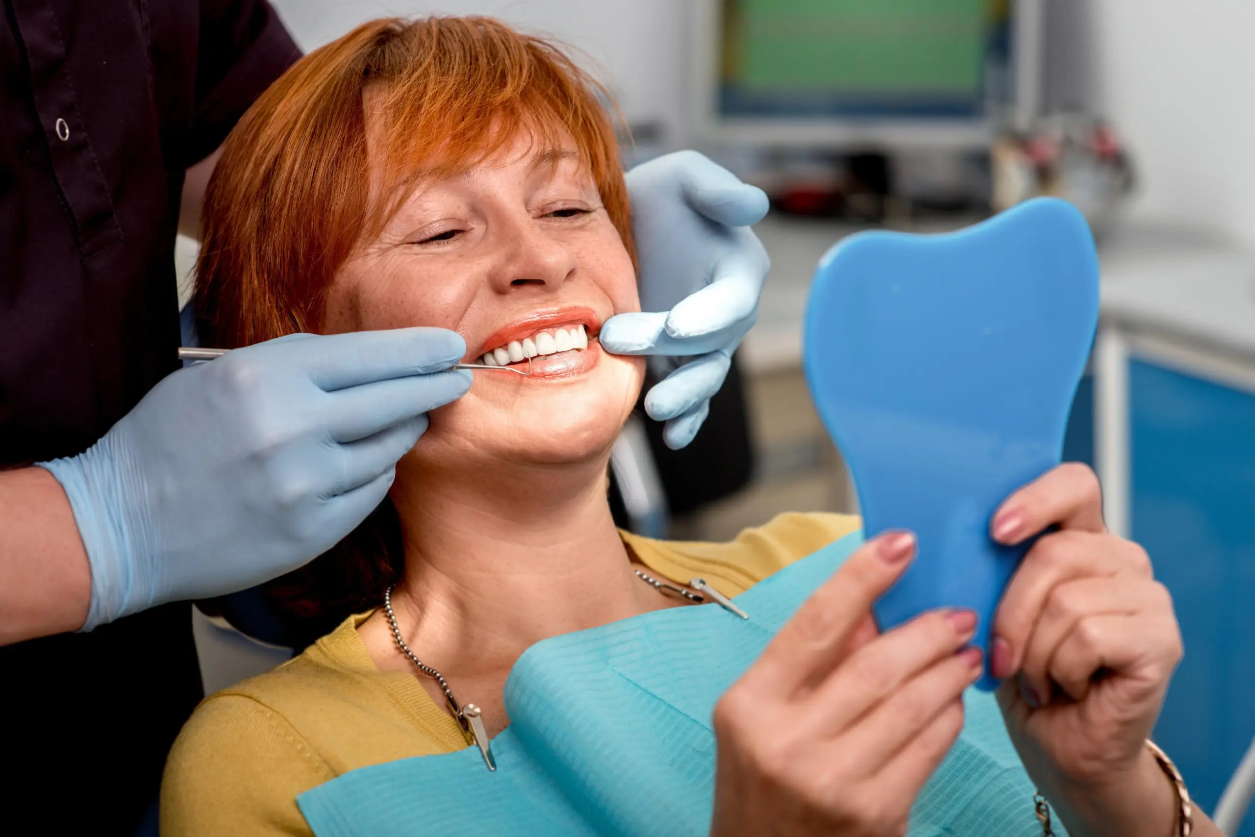 FollowupAdjustments truewhite Dentist with blue gloves examining patients teeth using a dental mirror
