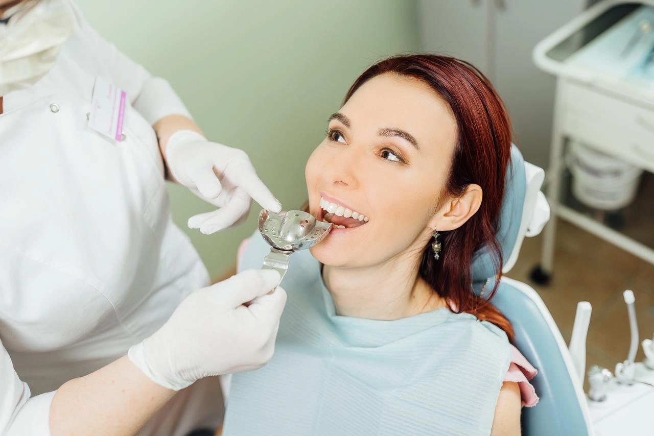 ImpressionsBiteRecording truewhite Woman patient seated in a dental chair while dentist examines her teeth with a mirror tool